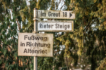 Fototapeta premium Verwitterte Wegweiser Rieter Steige Fußweg nach Altenriet vor Nadelbaum in Neckartenzlingen