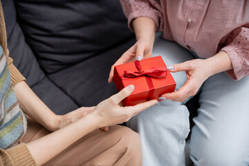 cropped view of woman presenting gift to mature mother on couch at home.