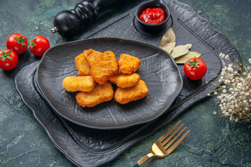 Close up view of chicken nuggets on a black plate and elegant fork ketchup on dark color tray white flower tomatoes with stem