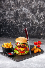 Delicious homemade sandwich and chicken nuggets fries ketchup fork on black board tomatoes with stem on gray ice background