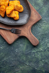 Half shot of chicken nuggets on a black plate and fork on wooden cutting board on the right side on dark background with free space