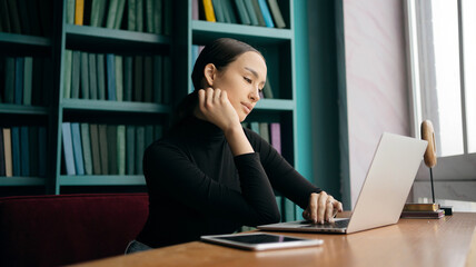 A woman sits at a desk in front of a bookcase with a bookcase behind her.