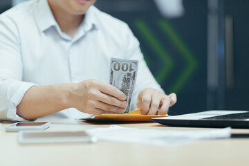 Close-up photo. Hands of a young man putting cash, dollars in a wallet, counting money in the...