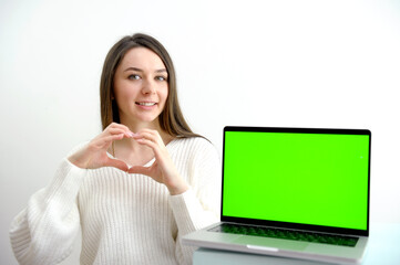 Young woman speak with friends on video call and shows heart with hands on camera from home office. Virtual party meeting team teleworking. Remote conference Computer green screen view. - Powered by Adobe