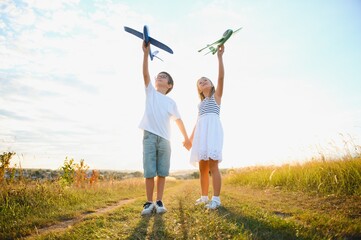 Running boy and girl holding two green and blue airplanes toy in the field during summer sunny day © Serhii