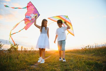 Happy children launch a kite in the field at sunset. Little boy and girl on summer vacation.
