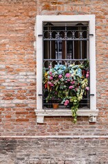 Fototapeta na wymiar Narrow window on a brick wall with a bunch of flowers on the window grille.