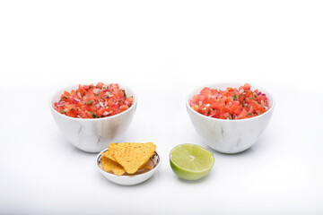 Fototapeta na wymiar 2 identical bowls containing freshly made salsa with a bowl of tortilla chips and a half slice of fresh lime