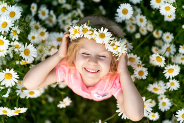 Little happy girl in daisies, close-up portrait on top, child smiling