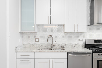 Fototapeta na wymiar A beautiful white kitchen detail shot with a tiled backsplash, white cabinets, stainless steel appliances, and marble countertop.