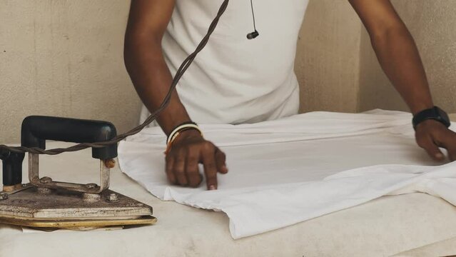 A man ironing a white t-shirt with an old iron, India