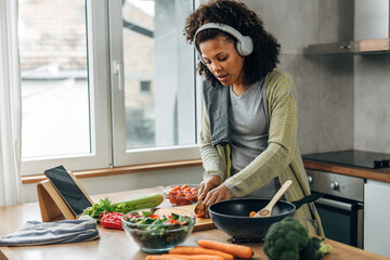 A multiracial woman with headphones is cooking in the kitchen