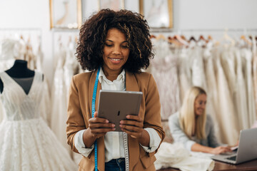 A beautiful multiracial woman looks at the tablet. She works in a bridal salon.