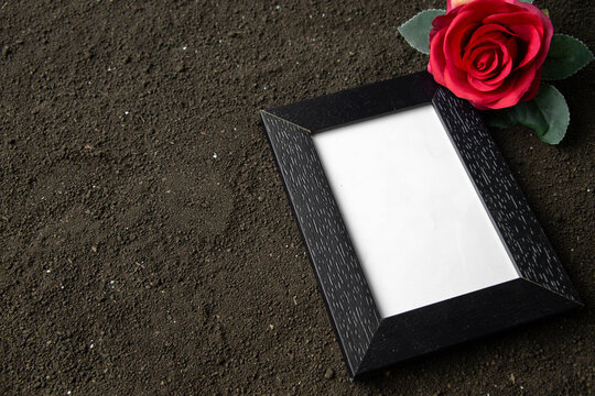 front view of empty picture frame with red flower on dark soil grim reaper death funeral