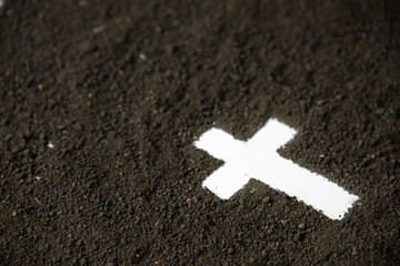 front view of white cross shape with dark soil death grim reaper funeral