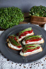 Top view of sandwiches for breakfast with slice of whole grain bread, cream cheese, mixed microgreens  and roasted pepper on grey plate on wooden table.