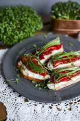 Closed image of sandwiches for breakfast with slice of whole grain bread, cream cheese, mixed microgreens  and roasted red pepper garnished on grey plate on wooden table.