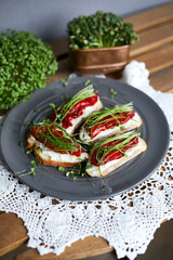 Top view of sandwiches for breakfast with slice of whole grain bread, cream cheese, mixed microgreens  and roasted red pepper garnished on grey plate on wooden table.