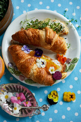Top view of a croissant with orange jam and cream cheese and with avocado, microgreens on a white plate, pansies, fruits. 