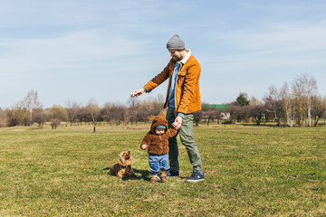 young father with toddler child playing with spaniel dog in the park