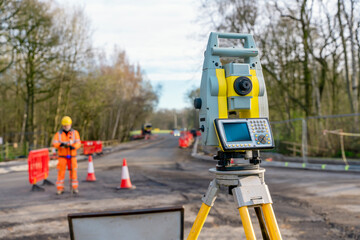 Site engineer operating his instrument during roadworks. Builder using total positioning station tachymeter on construction site for new road setting out