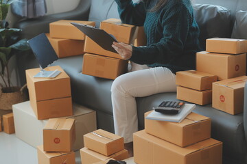 Fototapeta premium Startup SME small business entrepreneur of freelance Asian woman wearing apron using laptop and box to receive and review orders online to prepare to pack sell to customers, online sme business ideas.