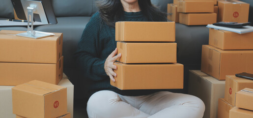 Startup SME small business entrepreneur of freelance Asian woman wearing apron using laptop and box to receive and review orders online to prepare to pack sell to customers, online sme business ideas.