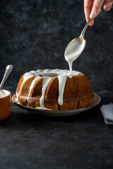 Bundt cake. Drizzling icing on homemade pound, cake. Dark background.