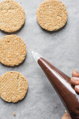 Piping chocolate ganache on oat cookies, piping dark chocolate filling on oatmeal cookies