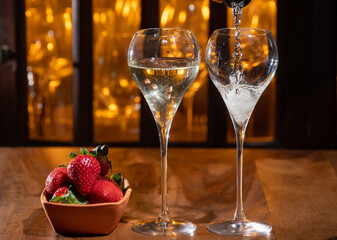 Glass of brut champagne bubbles wine in tulip glass and bowl with fresh strawberries on evening bar lights background