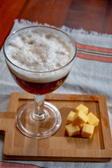 Glass of Belgian abbey brown beer and wooden board with old belgian cheese made by monks from cow...