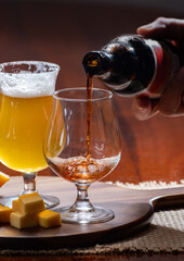 Glasses of Belgian yellow blond and dark brown beer made in abbey and wooden board with variety of belgian cheeses