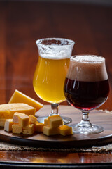 Glasses of Belgian yellow blond and dark brown beer made in abbey and wooden board with variety of belgian cheeses