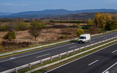 White delivery van on the highway. White modern delivery small shipment cargo courier van moving fast on motorway road to city urban suburb. The business distribution and logistics express service.
