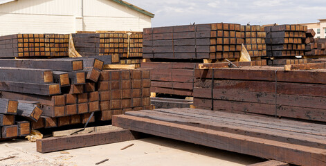 stacked piles of new railroad ties also called railway sleepers with anti-split plates on the ends - obrazy, fototapety, plakaty