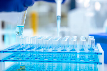 Unrecognizable scientist dripping blue liquid from pipette into test tube at table in laboratory.