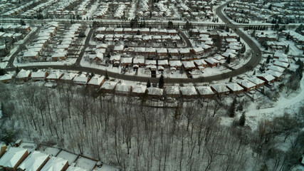 An aerial drone shot of a creek running through a forest with houses on the side during winter