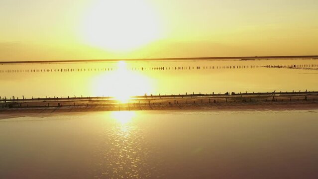 Sunset, dramatic and majestic sky over beach with sun reflection in water. Wood posts for salt extraction of extremely salty lake, Ukraine. Summer season, idyllic peaceful dusk sunlight.