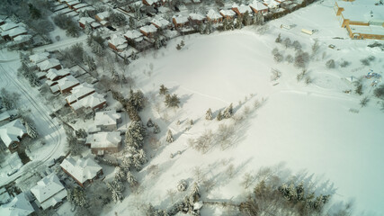 An aerial drone shot of houses and a park covered in snow in the winter
