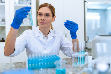 Woman researcher working with medical samples, holding test tube with blue liquid.
