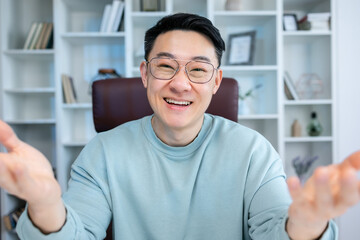 Friendly happy young asian man waving hand saying hello looking at camera greeting distant friend making online call, cheerful male vlogger blogger recording vlog teaching e-coaching via webcam © Ivan