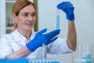 Woman researcher working with medical samples, holding test tube with blue liquid.