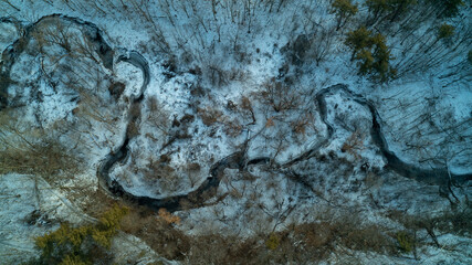 An aerial drone shot of a creek running through a forest during a winter sunrise