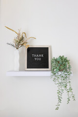 thank you on a black and tan letter board sitting on a floating shelf with plants. modern home decor