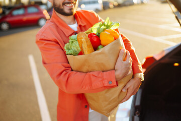 
Stylish man with paper bags of vegetarian products in the parking lot near his car. Shopping for...