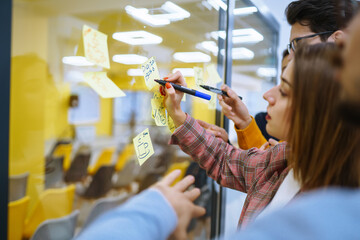 Modern group of people sharing ideas concept with paper note writing strategy in office. Business colleagues write stickers on the glass wall standing in the office. Brainstorming concept.