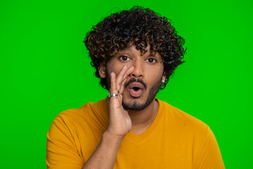 Fototapeta na wymiar Keep my secrets, silence. Indian man whisper news rumors holding hands near mouth, share gossip, quiet. Hindu guy telling interesting confidential story isolated on green chroma key background indoors