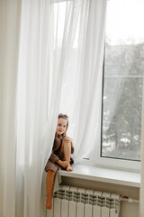 Portrait of a little girl in a brown dressing gown, who is sitting on the windowsill