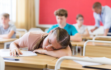 Fototapeta na wymiar Teenager students sitting at desks and listening. Girl sleeping on desk.