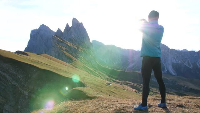 Young man in sport trail clothes stretching on Seceda mountain peak at sunrise. Puez Odle, Trentino, Dolomites, Italy.